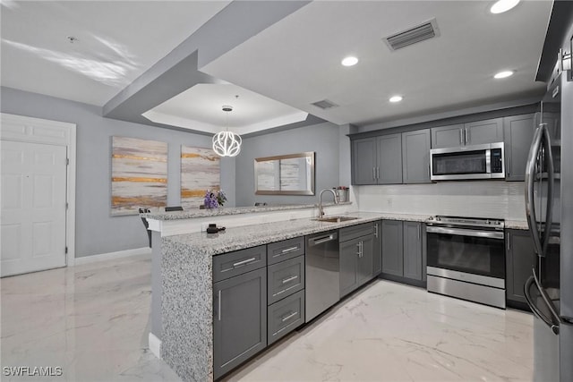 kitchen featuring appliances with stainless steel finishes, sink, gray cabinetry, kitchen peninsula, and a raised ceiling