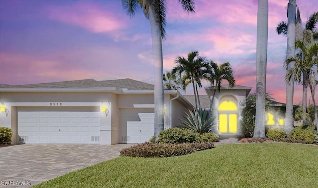 view of front of home featuring a garage, a front lawn, decorative driveway, and stucco siding