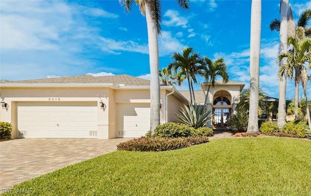 view of front of house featuring a garage, french doors, decorative driveway, stucco siding, and a front lawn