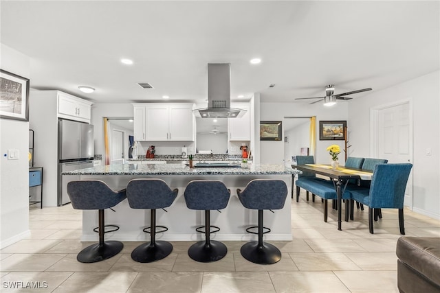 kitchen featuring white cabinets, a kitchen breakfast bar, freestanding refrigerator, light stone countertops, and island exhaust hood