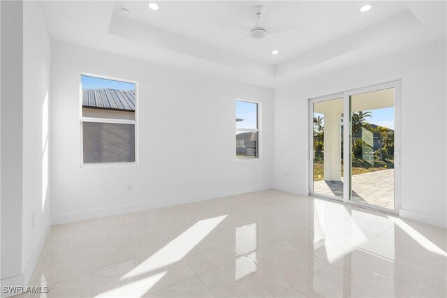 tiled empty room featuring ceiling fan and a tray ceiling