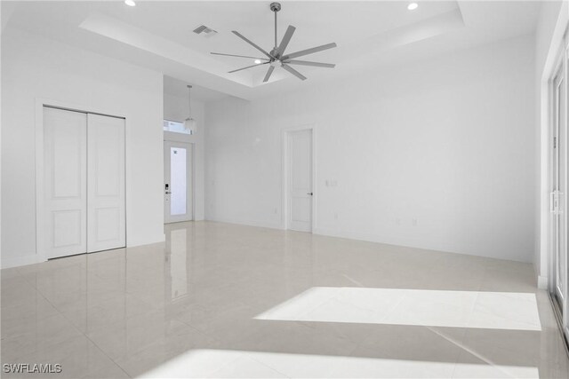 empty room with a tray ceiling, ceiling fan, and a high ceiling