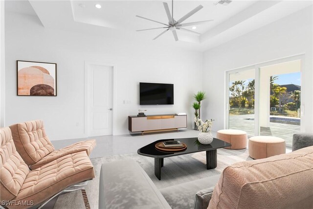 living room with a towering ceiling, ceiling fan, and a tray ceiling