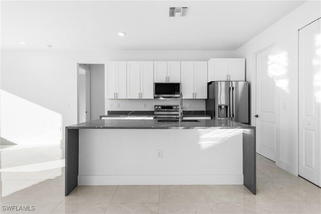 kitchen featuring sink, dark stone counters, an island with sink, stainless steel appliances, and white cabinets