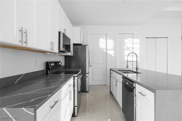 kitchen with sink, appliances with stainless steel finishes, dark stone countertops, white cabinets, and a center island with sink