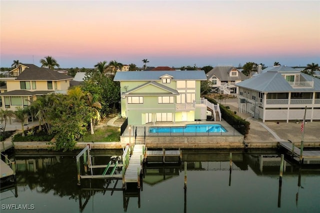 back house at dusk featuring a balcony, a water view, and a patio area