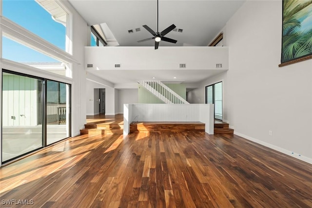 unfurnished living room with ceiling fan, a healthy amount of sunlight, wood-type flooring, and a high ceiling