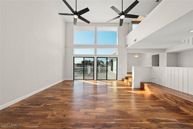 unfurnished living room featuring ceiling fan, visible vents, wood finished floors, baseboards, and a high ceiling
