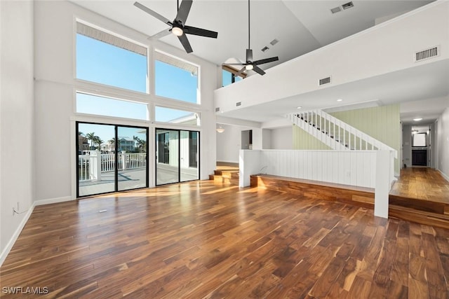 unfurnished living room with visible vents, a ceiling fan, wood finished floors, and a towering ceiling