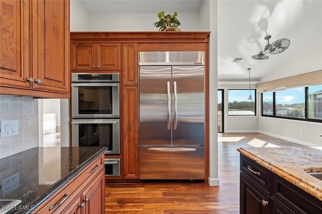 kitchen with tasteful backsplash, dark stone countertops, appliances with stainless steel finishes, pendant lighting, and hardwood / wood-style floors