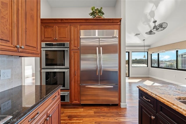 kitchen featuring dark stone counters, backsplash, stainless steel appliances, and dark wood-style flooring