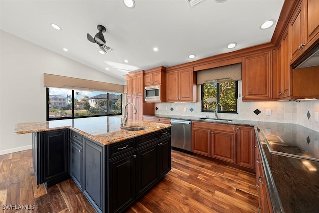 kitchen with lofted ceiling, sink, appliances with stainless steel finishes, light stone countertops, and an island with sink