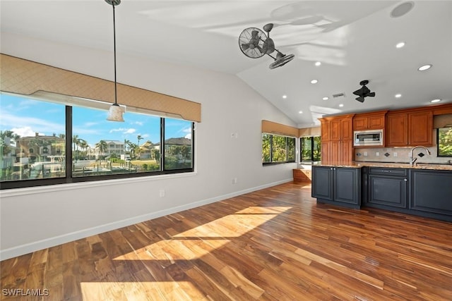 kitchen featuring pendant lighting, stainless steel microwave, light stone countertops, a healthy amount of sunlight, and vaulted ceiling