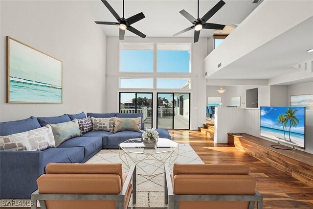 living area featuring a towering ceiling, a ceiling fan, visible vents, and wood finished floors