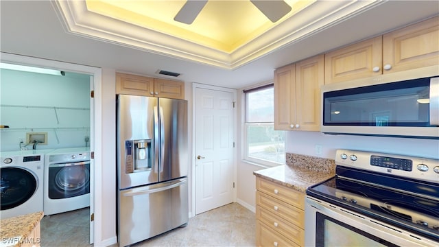 kitchen featuring independent washer and dryer, a tray ceiling, stainless steel appliances, light stone countertops, and light brown cabinets