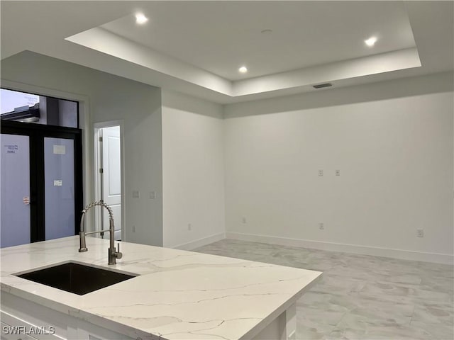 kitchen featuring sink, light stone counters, and a tray ceiling