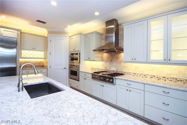 kitchen with light stone counters, a sink, visible vents, appliances with stainless steel finishes, and wall chimney exhaust hood