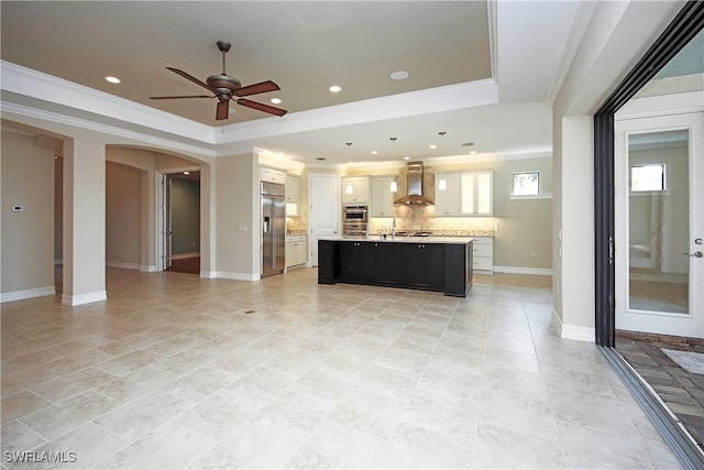 kitchen with arched walkways, a tray ceiling, light countertops, stainless steel built in fridge, and wall chimney range hood