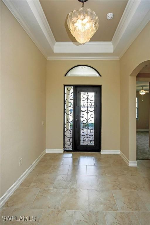 foyer featuring ornamental molding, arched walkways, a raised ceiling, and baseboards