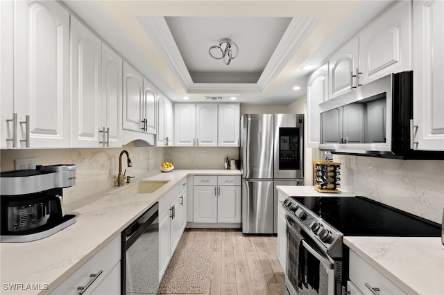 kitchen with white cabinetry, appliances with stainless steel finishes, a tray ceiling, and light stone counters