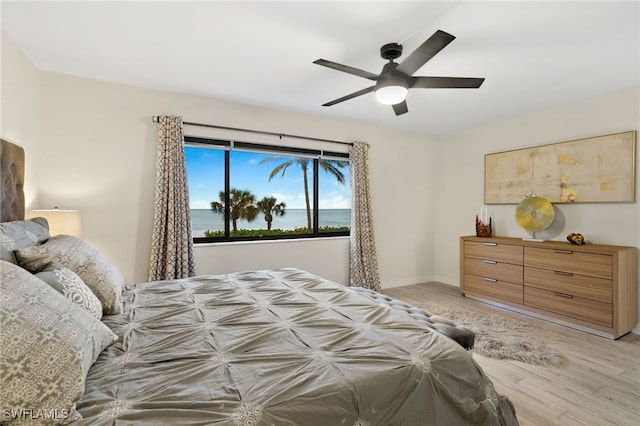 bedroom featuring light hardwood / wood-style flooring, ceiling fan, and a water view