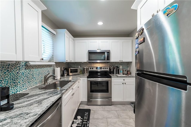 kitchen with appliances with stainless steel finishes, white cabinetry, sink, backsplash, and light stone countertops