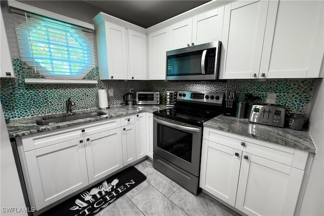 kitchen with white cabinetry, sink, stainless steel appliances, and dark stone countertops