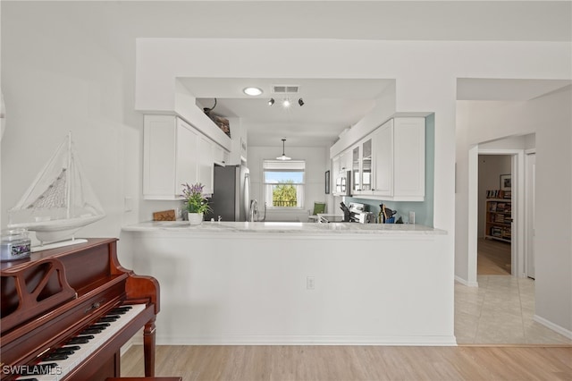 kitchen with white cabinetry, hanging light fixtures, stainless steel appliances, kitchen peninsula, and light wood-type flooring