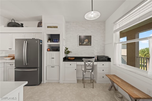 kitchen featuring stainless steel fridge, white cabinetry, built in desk, and decorative light fixtures