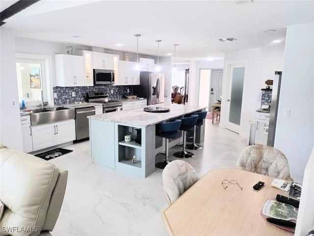 kitchen with white cabinetry, stainless steel appliances, decorative light fixtures, and a center island