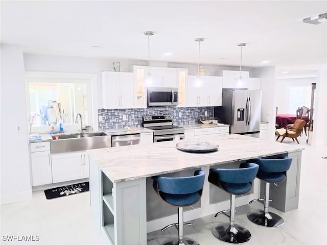 kitchen with sink, a breakfast bar, hanging light fixtures, stainless steel appliances, and white cabinets