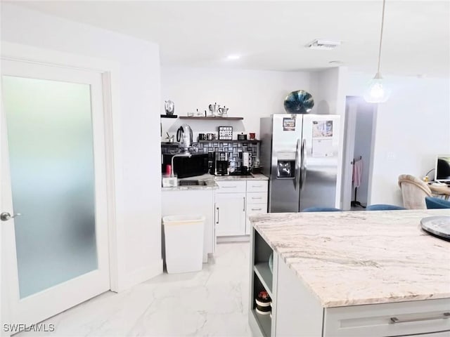 kitchen featuring white cabinetry, hanging light fixtures, stainless steel fridge, and light stone countertops