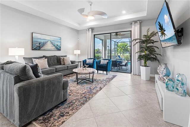 living room featuring a raised ceiling, light tile patterned floors, and ceiling fan