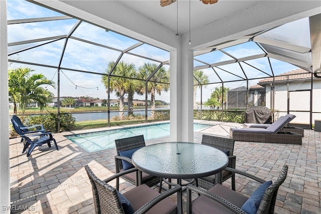 view of patio featuring glass enclosure, an outdoor pool, a water view, and ceiling fan