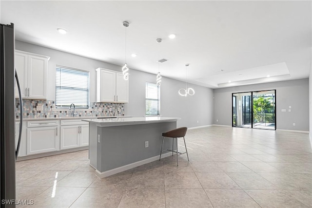 kitchen with open floor plan, freestanding refrigerator, decorative backsplash, a kitchen island, and light tile patterned floors