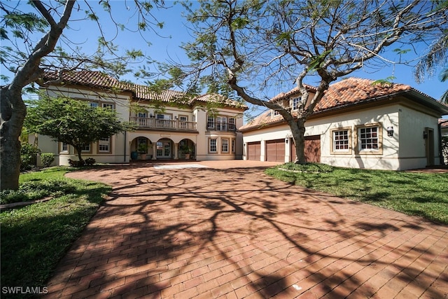 rear view of property featuring a garage, a balcony, a tiled roof, a yard, and stucco siding