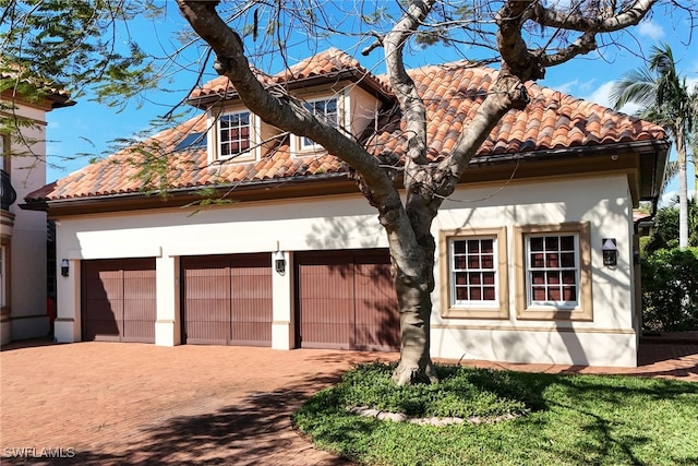 mediterranean / spanish home featuring a garage, a tile roof, and decorative driveway