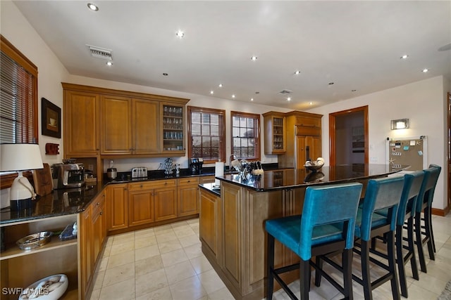 kitchen featuring visible vents, a kitchen island, glass insert cabinets, a breakfast bar, and paneled built in refrigerator