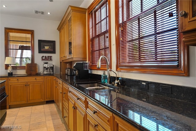 kitchen with glass insert cabinets, dark stone counters, visible vents, and a sink