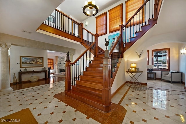 stairway with visible vents, baseboards, a towering ceiling, ornate columns, and a fireplace