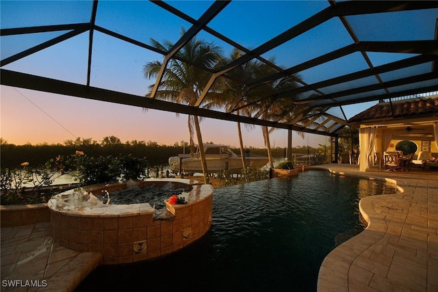 pool at dusk featuring a lanai, a patio area, and a pool with connected hot tub