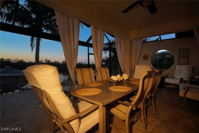 patio terrace at dusk featuring a water view, ceiling fan, and outdoor dining space