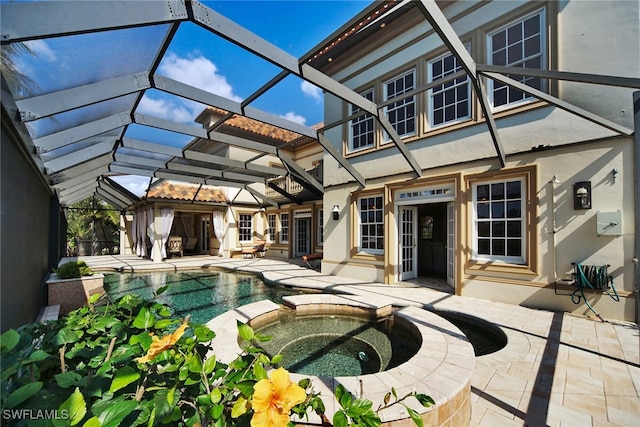 back of property with a lanai, a patio area, a pool with connected hot tub, and stucco siding