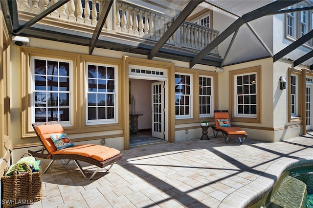 view of patio with a balcony, glass enclosure, and an outdoor pool