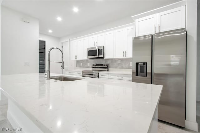 kitchen with sink, a center island with sink, appliances with stainless steel finishes, light stone countertops, and white cabinets