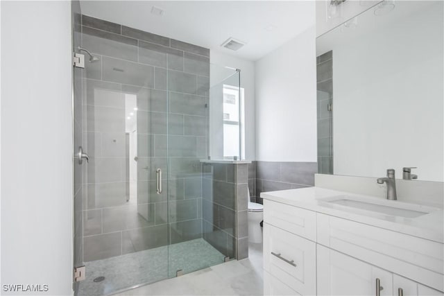 bathroom with vanity, toilet, a shower with door, and tile walls