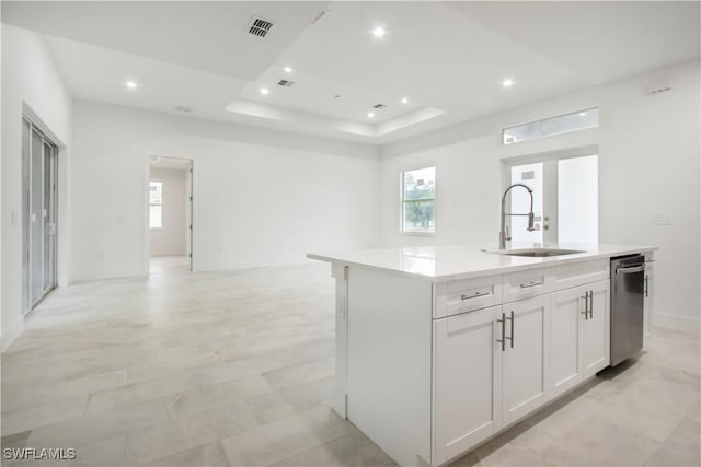 kitchen with sink, stainless steel dishwasher, a tray ceiling, an island with sink, and white cabinets