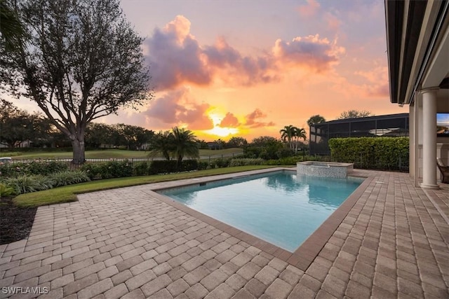 pool at dusk featuring a patio area and an in ground hot tub