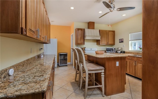 kitchen featuring a breakfast bar area, light stone countertops, a kitchen island, custom exhaust hood, and beverage cooler