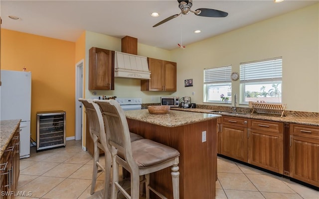 kitchen with white appliances, a kitchen breakfast bar, wine cooler, light stone countertops, and custom exhaust hood